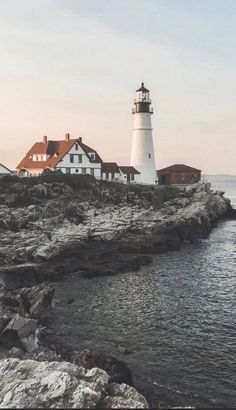 a light house sitting on top of a rocky cliff next to the ocean with houses in the background