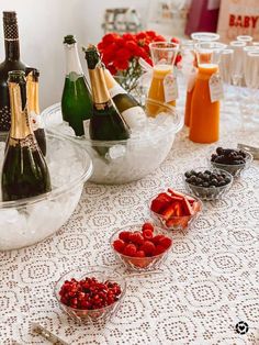 several bottles of champagne and berries on a table with bowls of fruit in the foreground