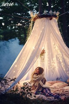 a woman sitting in front of a white tent with fairy lights hanging from the ceiling