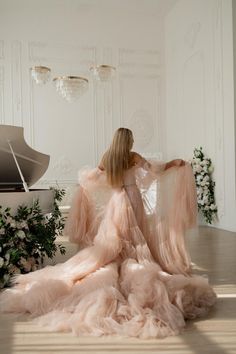 a woman sitting on the floor in front of a piano wearing a long pink dress