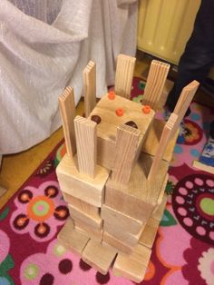 a wooden toy castle made out of wood blocks on a colorful rug in front of a white curtain