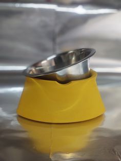 two metal bowls sitting on top of a yellow stand with a silver bowl in the middle