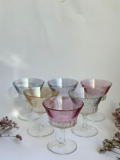 four wine glasses sitting next to each other on top of a white tablecloth with dried flowers in the background