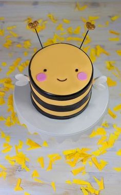 a cake with a bee on it sitting on top of a table covered in yellow confetti