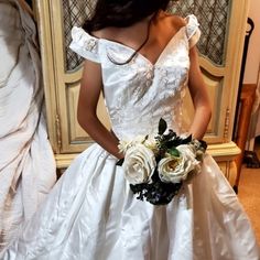 a woman in a white wedding dress standing next to a dresser with flowers on it