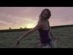 a woman standing in a field with her arms out and the sun setting behind her