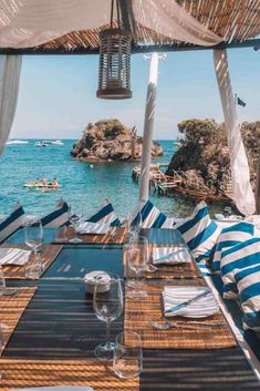 an outdoor dining area overlooking the ocean with blue and white striped tablecloths, place settings and water