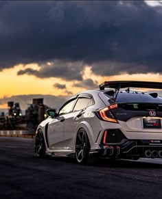 the rear end of a white honda civic type car with dark clouds in the background