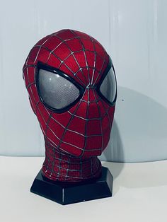 a spider - man mask is sitting on top of a black stand with white walls behind it