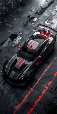 an aerial view of a black sports car with red paint streaks on the hood and side stripes