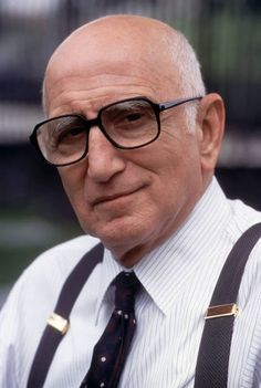 an older man with glasses and suspenders looks at the camera while wearing a striped shirt