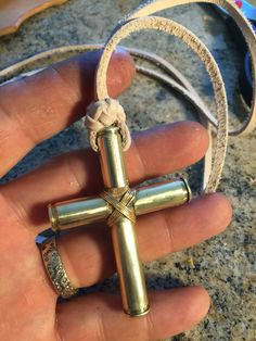 a hand holding a cross pendant on top of a leather cord with two rings around it