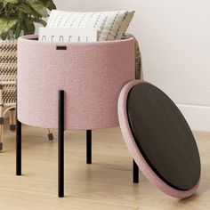 a pink and black ottoman sitting on top of a wooden floor next to a potted plant