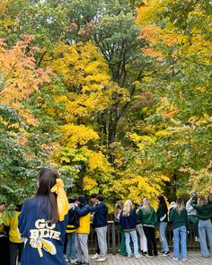 a group of people standing on top of a wooden bridge next to trees with yellow leaves