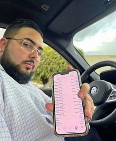 a man sitting in a car holding up a cell phone