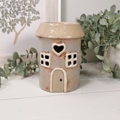 a ceramic pot with a heart shaped window on it next to some plants and a framed photo