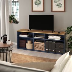 a flat screen tv sitting on top of a wooden shelf in a living room next to a window