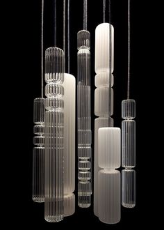 several clear glass vases hanging from strings on a black background with one candle in the middle