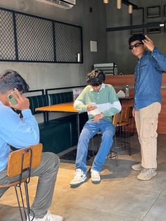 three men are sitting at tables and one man is on his cell phone while the other man holds up a piece of paper