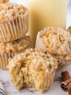 some muffins are sitting on a marble table with cinnamon sticks and a glass of milk