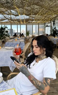 a tattooed woman sitting at a table looking at her phone