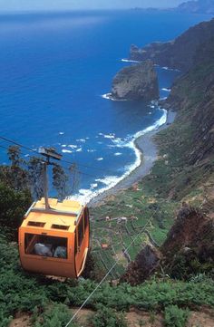 an orange cable car going up the side of a mountain next to the ocean on a sunny day