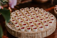 there are many small heart shaped desserts on the wooden platter with flowers in the background