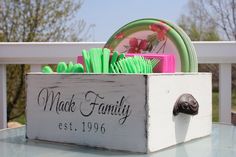 a wooden box filled with green and pink items on top of a glass table next to a white fence