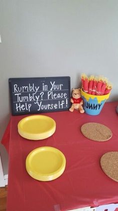 a red table topped with yellow plates and bowls filled with food next to a chalkboard sign