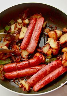 sausages and potatoes being cooked in a skillet with tongs on the side