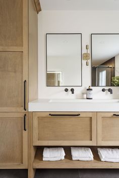 a bathroom with two sinks and mirrors on the wall next to wooden cupboards in front of it