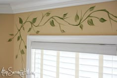 green leaves painted on the side of a wall above a window in a room with white shutters