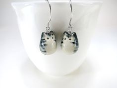 a pair of white and black cat shaped earrings on a white cup with silver earwires