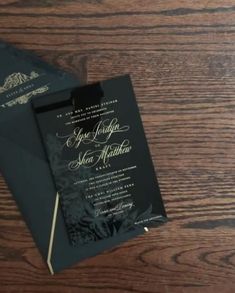 two black and gold wedding cards on top of a wooden table