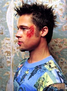 a young man with red paint on his face and hair is standing in front of a wall