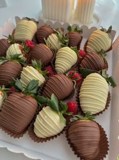 chocolate covered strawberries are arranged on a white platter next to a lit candle