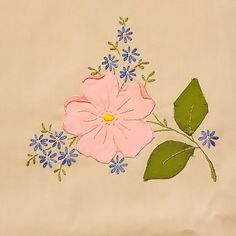 a pink flower with green leaves and blue flowers on a beige background is embroidered onto the fabric