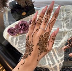 a woman's hand with henna tattoos on it and flowers in the background