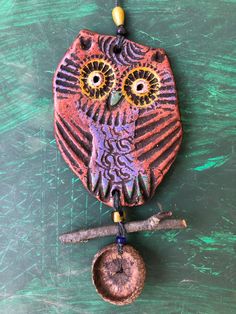 an owl is hanging from a chain on a green surface with a piece of wood