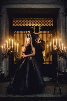 a man and woman dressed in black standing next to each other with candles behind them