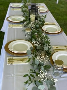 the table is set with white and gold plates, silverware, greenery, and candlesticks