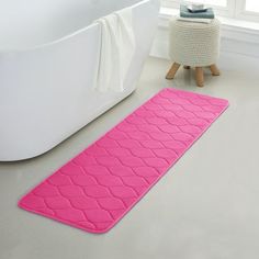 a pink bath mat sitting on top of a bathroom floor next to a white tub