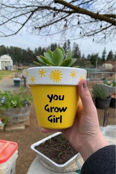 a person holding up a yellow pot with a plant in it that says you grow girl