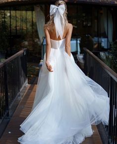 a woman in a white wedding dress walking across a bridge with her back to the camera