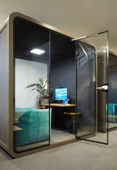 an office cubicle with glass walls and a desk in the corner, surrounded by blue couches