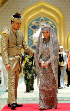 a man and woman in wedding attire standing next to each other on a red carpet