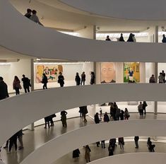 many people are walking around in an art museum with paintings on the walls and stairs