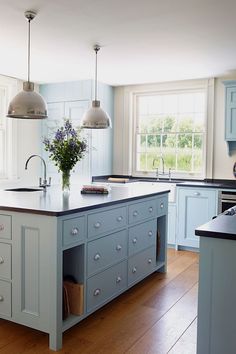 a kitchen with blue cabinets and an island in the middle is decorated with purple flowers