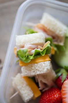 a plastic container filled with sandwiches and strawberries