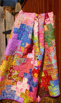 a multicolored quilt hanging on a wooden fence